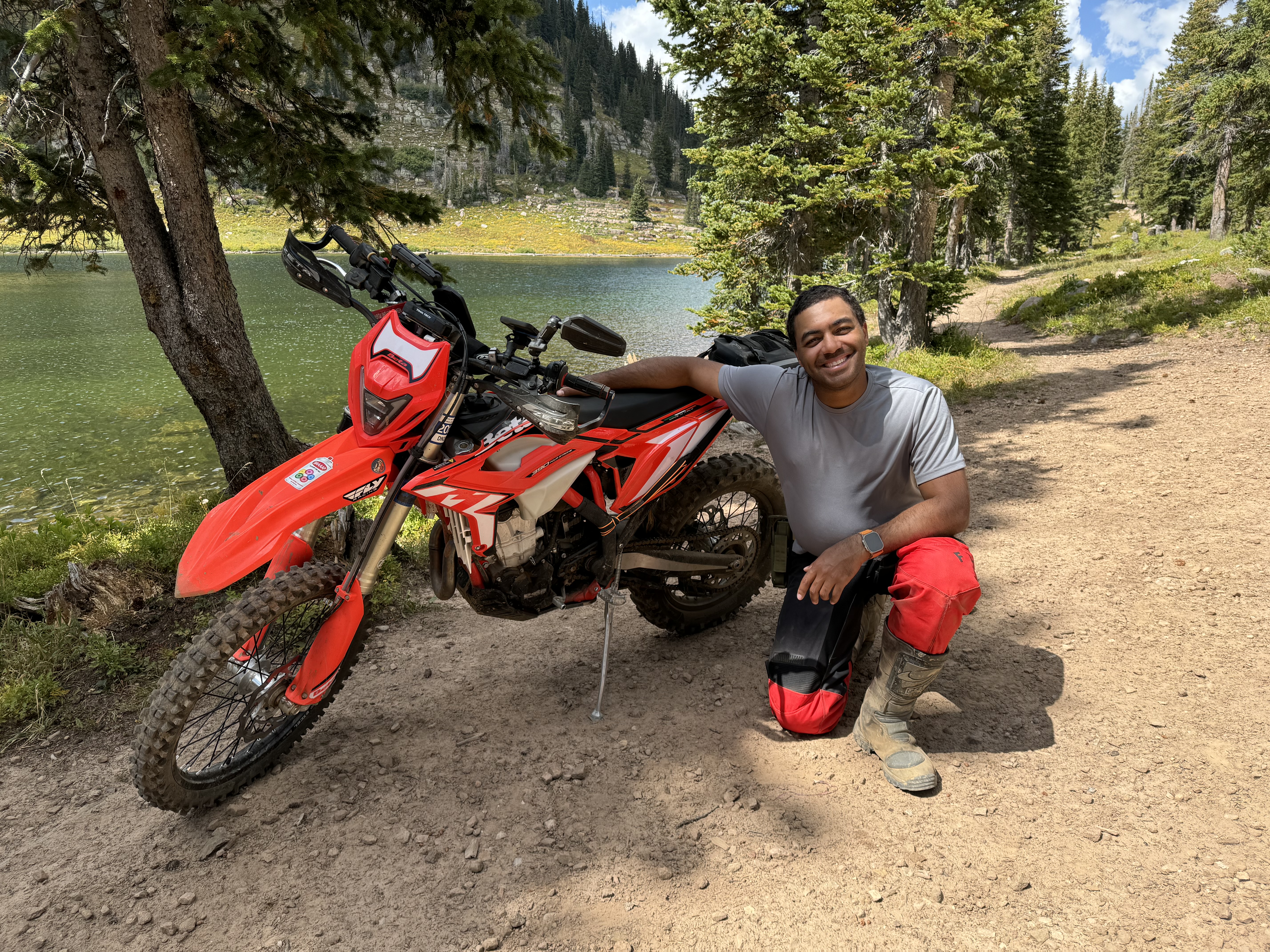 Dustin Holstein kneeling beside his red dirt bike on a trail next to Adam's Lake in Colorado.