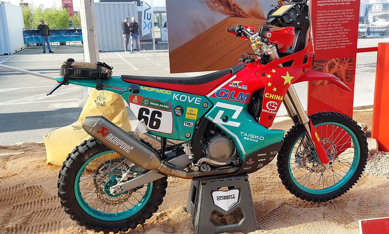 A teal and red Kove 450 Rally bike, race number 66, on a display stand